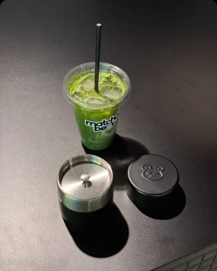 Iced matcha in a branded cup next to the Matcha Bear canisters